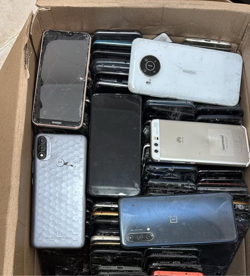 Box containing various used smartphones with different models and conditions.