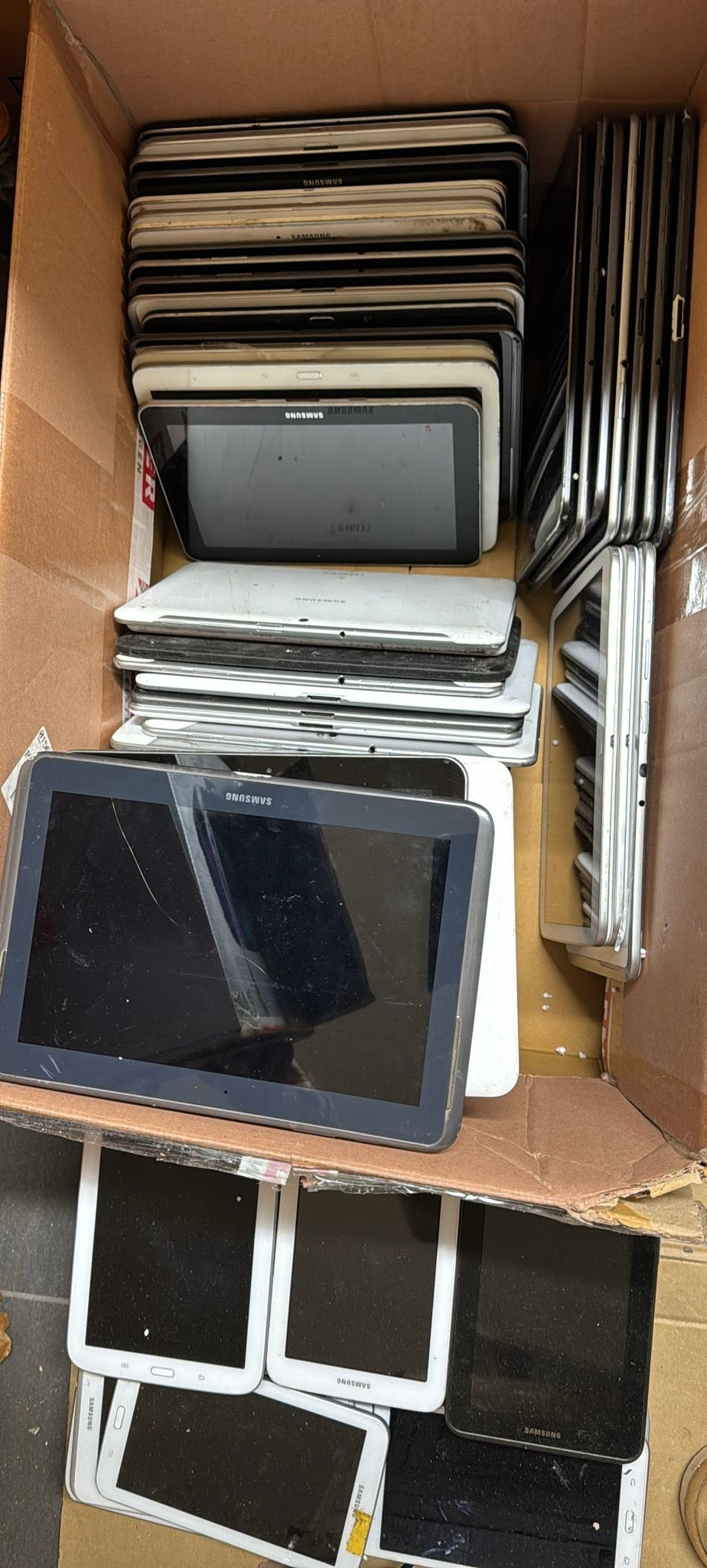 Collection of electronic devices, including tablets and monitors, in a cardboard box.